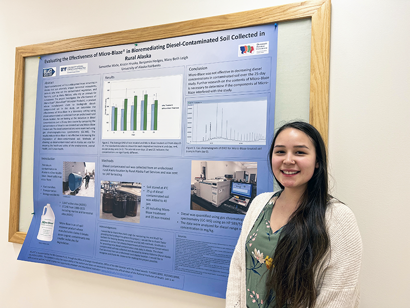 Samantha Wade stands in front of her research poster, “Evaluating the Effectiveness of Micro-Blaze in Bioremediating Diesel-Contaminated Soil Collected in Rural Alaska.”